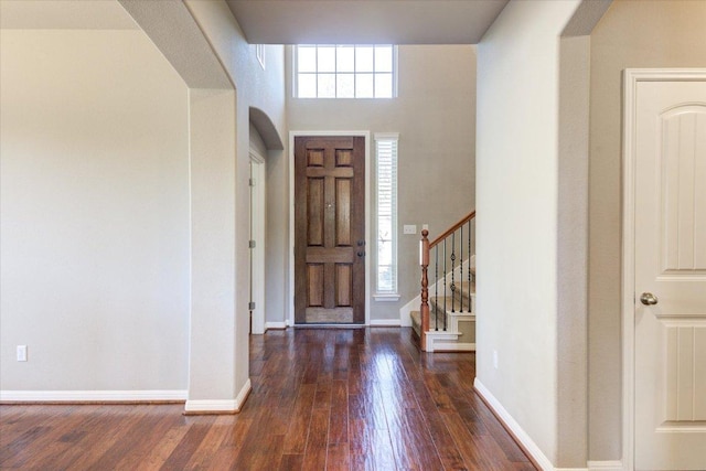 foyer entrance with arched walkways, a healthy amount of sunlight, baseboards, and hardwood / wood-style floors