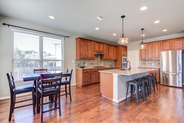 kitchen featuring visible vents, a sink, stainless steel appliances, under cabinet range hood, and brown cabinets