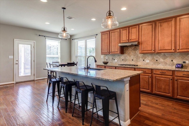 kitchen featuring visible vents, stainless steel gas cooktop, under cabinet range hood, brown cabinetry, and a sink