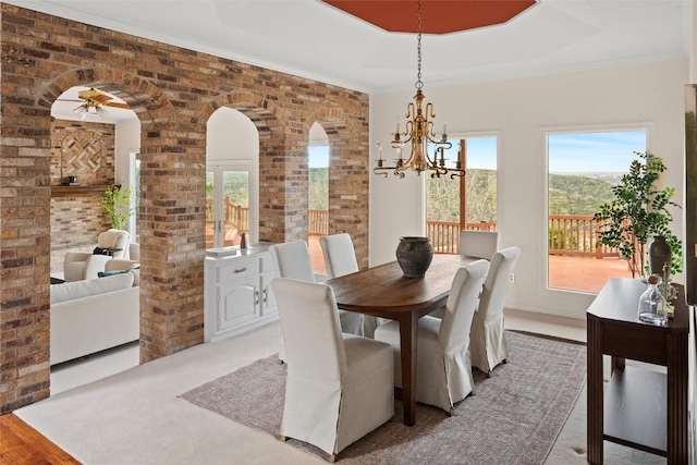 dining room featuring arched walkways, brick wall, ornamental molding, and ceiling fan with notable chandelier