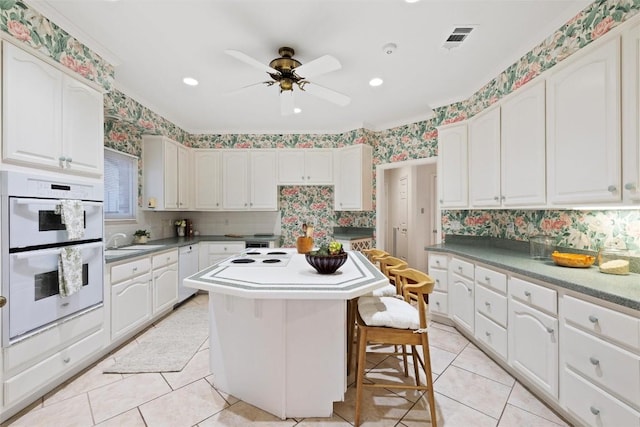 kitchen featuring visible vents, a center island, wallpapered walls, white cabinets, and white appliances