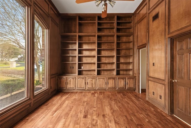 unfurnished room featuring light wood-style flooring, plenty of natural light, built in shelves, and ceiling fan