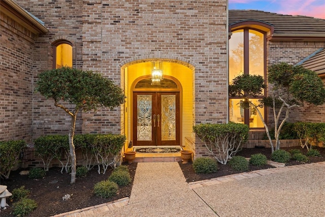 doorway to property featuring brick siding, french doors, and a tile roof