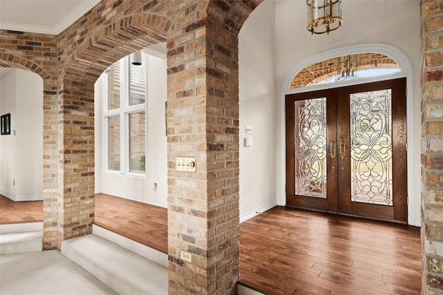 foyer entrance with a high ceiling, arched walkways, french doors, wood-type flooring, and a chandelier