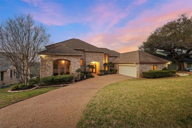 french country inspired facade featuring a garage, a lawn, concrete driveway, and a tiled roof