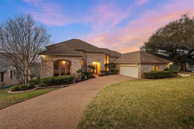 5315 Valburn Cir, Austin, TX 78731 - french country home with an attached garage, concrete driveway, a lawn, a tile roof, and brick siding