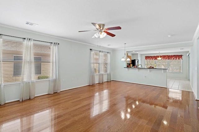 unfurnished living room with visible vents, wood finished floors, crown molding, and ceiling fan with notable chandelier