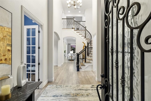 foyer entrance with wood finished floors, baseboards, an inviting chandelier, arched walkways, and stairs