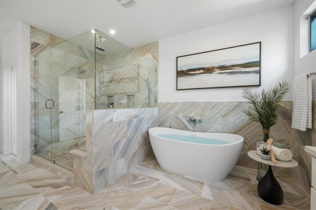 bathroom with a shower stall, a freestanding tub, and tile walls