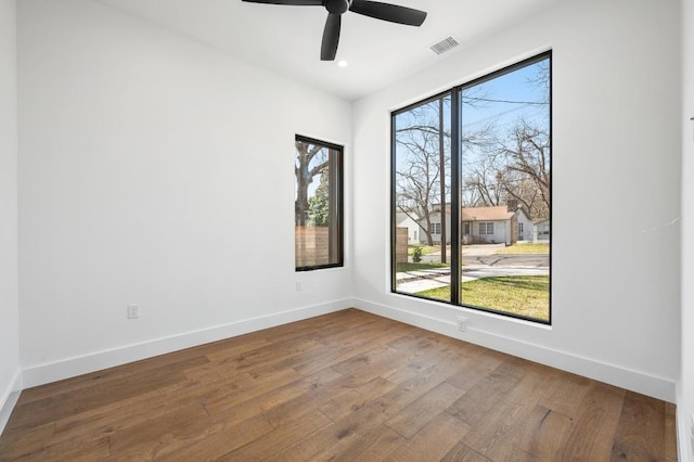 empty room with visible vents, wood-type flooring, baseboards, and a ceiling fan