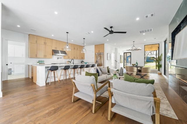 living room with light wood-type flooring, visible vents, recessed lighting, and ceiling fan with notable chandelier