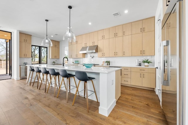 kitchen with light brown cabinets, visible vents, light wood-style flooring, under cabinet range hood, and built in fridge