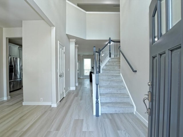 foyer with stairway, baseboards, a high ceiling, and light wood-style floors