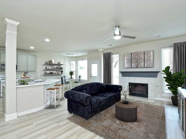 living area with visible vents, light wood-style floors, ceiling fan, and a tiled fireplace