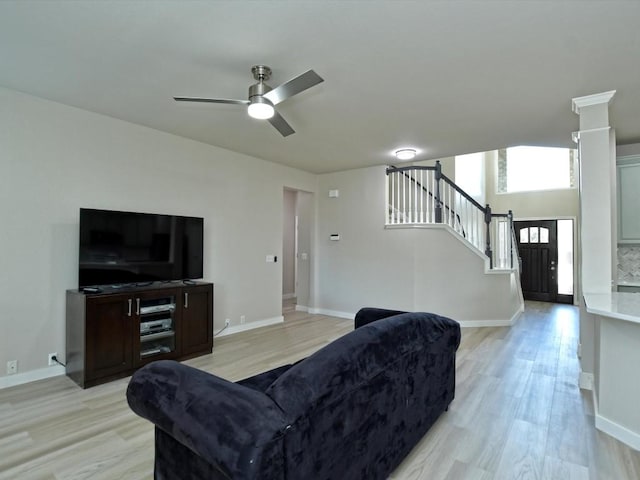 living area featuring stairway, baseboards, light wood-style flooring, and a ceiling fan