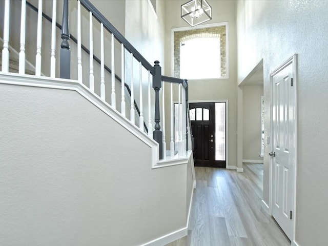 entrance foyer with a notable chandelier, wood finished floors, stairway, a high ceiling, and baseboards