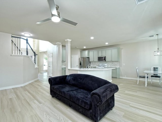 living room with stairway, baseboards, visible vents, light wood finished floors, and ceiling fan