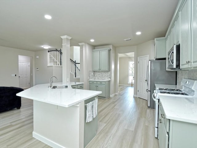 kitchen featuring white range with gas cooktop, a large island with sink, a sink, decorative backsplash, and stainless steel microwave