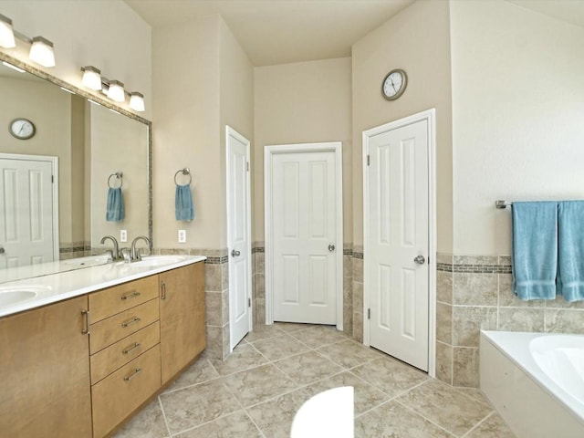 full bath featuring a garden tub, double vanity, wainscoting, tile walls, and a sink