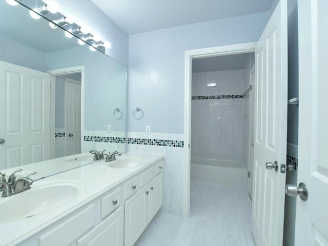 bathroom featuring double vanity, tile walls, shower / bath combination, and a sink