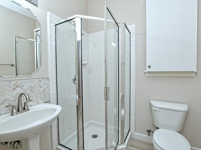 bathroom with a sink, backsplash, a stall shower, and toilet