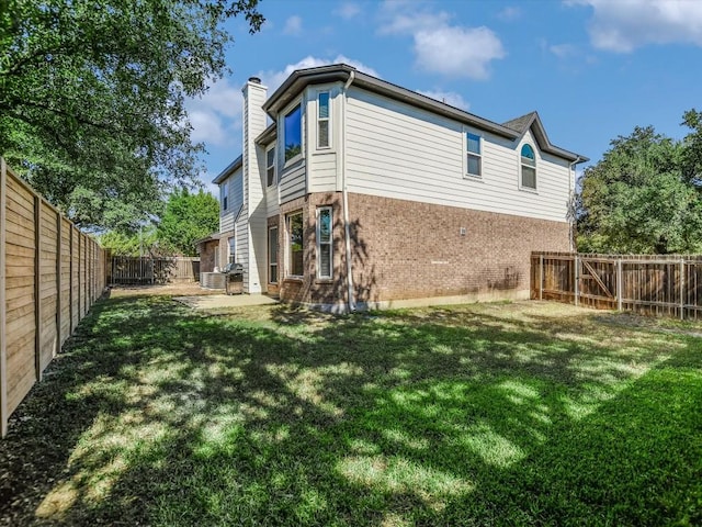 rear view of property featuring brick siding, a chimney, a fenced backyard, and a lawn