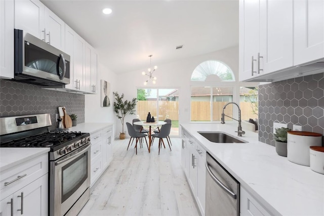 kitchen with vaulted ceiling, stainless steel appliances, a notable chandelier, white cabinetry, and a sink