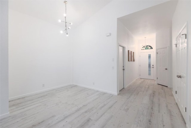 entryway featuring a notable chandelier, baseboards, light wood finished floors, and a towering ceiling