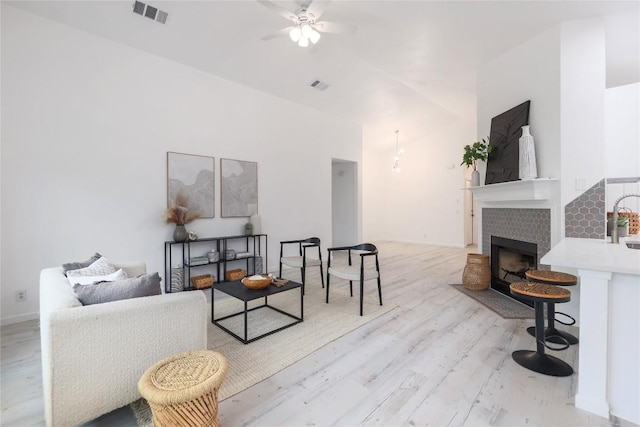 living area featuring visible vents, baseboards, a fireplace, light wood-style floors, and a ceiling fan