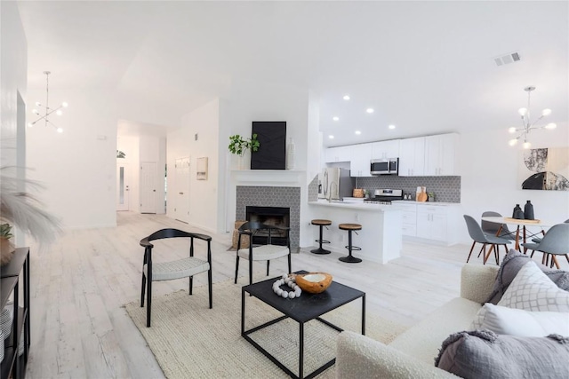 living room with visible vents, light wood-style flooring, a tile fireplace, and an inviting chandelier