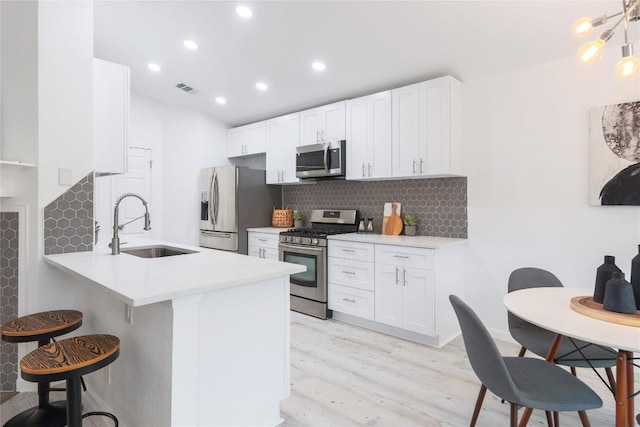 kitchen featuring a sink, backsplash, stainless steel appliances, a breakfast bar area, and white cabinets