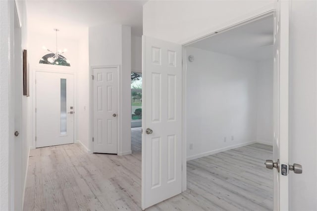 foyer entrance with baseboards, an inviting chandelier, and light wood-style flooring