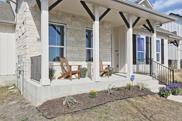 entrance to property featuring board and batten siding, covered porch, stone siding, and roof with shingles