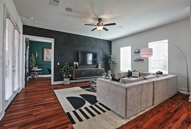 living area featuring visible vents, wood finished floors, baseboards, ceiling fan, and an accent wall