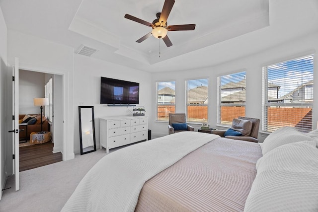 bedroom featuring a raised ceiling, multiple windows, visible vents, and light carpet