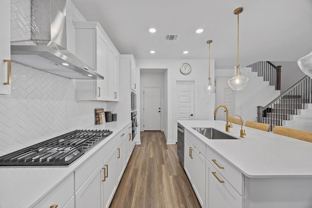 kitchen with visible vents, dark wood-type flooring, a sink, appliances with stainless steel finishes, and wall chimney exhaust hood