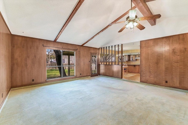 unfurnished living room featuring lofted ceiling with beams, carpet floors, wood walls, and a ceiling fan