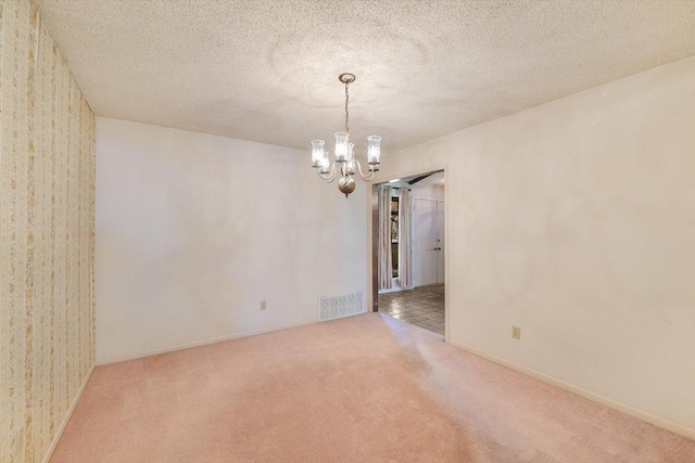 carpeted empty room with a notable chandelier, baseboards, visible vents, and a textured ceiling