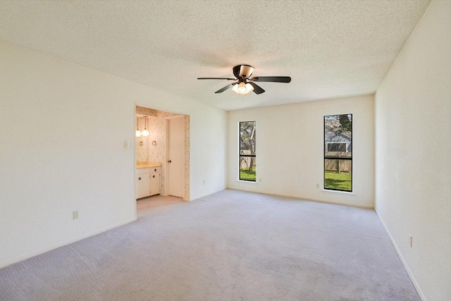 spare room with a textured ceiling, light colored carpet, baseboards, and ceiling fan