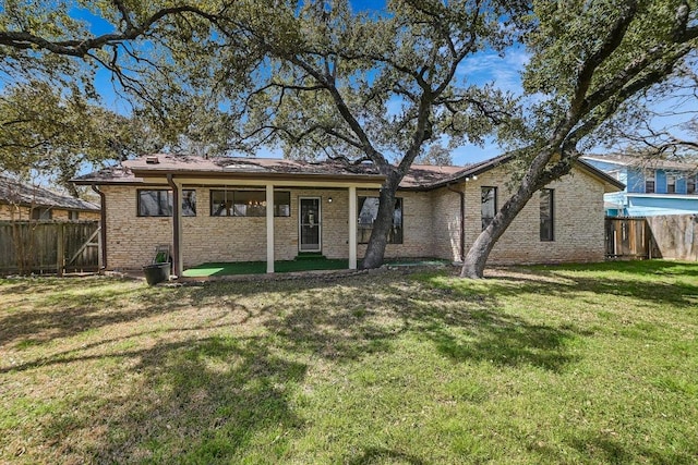 back of house featuring brick siding, fence, and a lawn