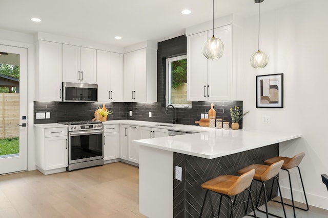 kitchen featuring a peninsula, a breakfast bar area, white cabinets, and appliances with stainless steel finishes