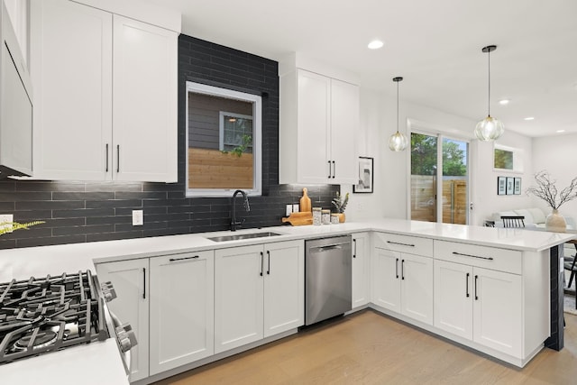 kitchen with light countertops, a peninsula, white cabinets, stainless steel appliances, and a sink