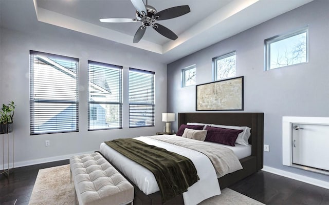 bedroom with dark wood finished floors, a tray ceiling, multiple windows, and baseboards