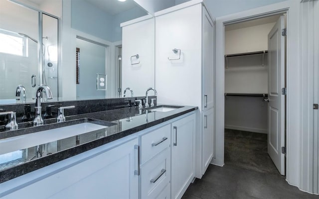 full bath featuring double vanity, a spacious closet, a stall shower, and a sink