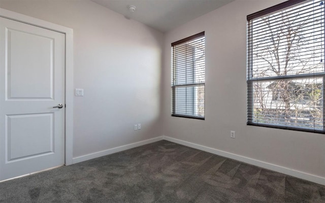 spare room with dark colored carpet, baseboards, and vaulted ceiling