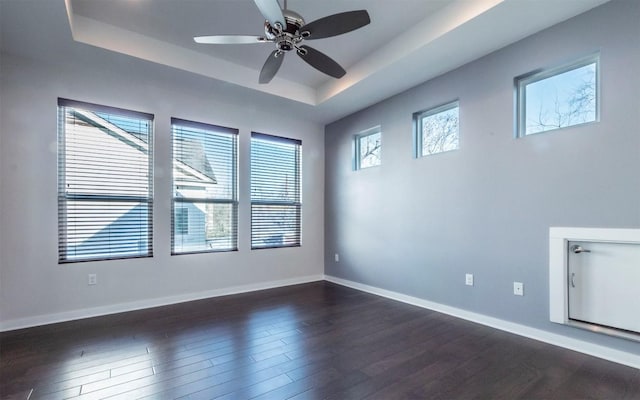 unfurnished room featuring a tray ceiling, baseboards, dark wood-style flooring, and ceiling fan