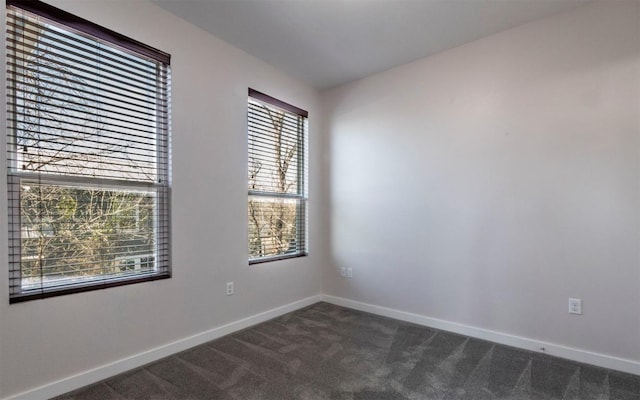 unfurnished room featuring dark carpet and baseboards