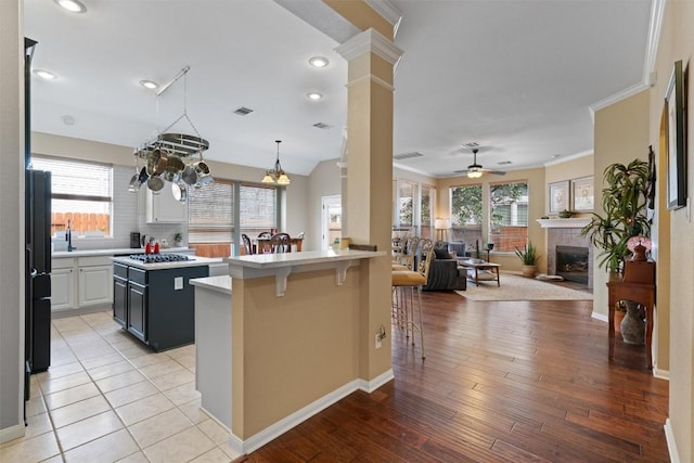 kitchen with a kitchen bar, ceiling fan with notable chandelier, a glass covered fireplace, freestanding refrigerator, and light countertops