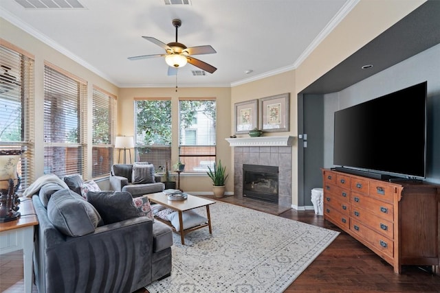 living area featuring dark wood-style floors, visible vents, a tile fireplace, ceiling fan, and crown molding