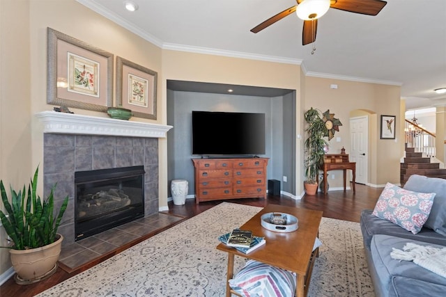 living area featuring wood finished floors, arched walkways, crown molding, ceiling fan, and stairs